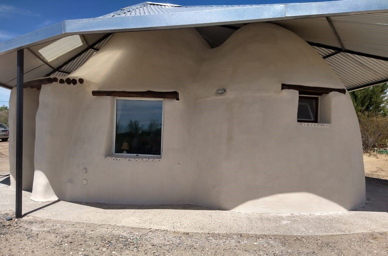Domo de superadobe con techo metálico entre arbustos de la estepa patagónica